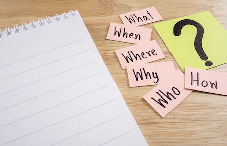 Questions what, when, where, why, who, how and white notebook on wood background